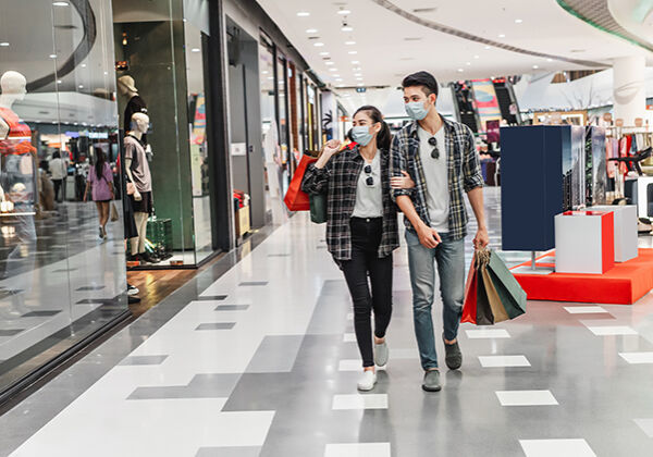 Young couple in protection mask holding multiple paper shopping bag walking in the corridor of large shopping mall, New normal lifestyle and shopping concept