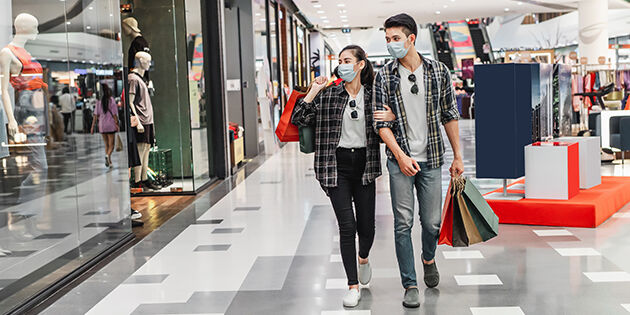 Young couple in protection mask holding multiple paper shopping bag walking in the corridor of large shopping mall, New normal lifestyle and shopping concept